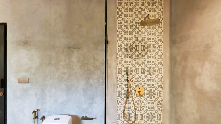 Detail of the rainfall shower area in The Mahaloka bathroom, showing patterned tiles and brass fixtures against polished concrete.