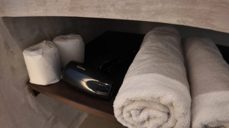 Bathroom shelf detail at The Mahaloka showing neatly rolled towels, spare toilet paper, and a hairdryer.