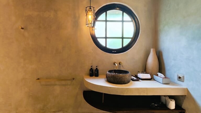 Close-up of the natural stone sink and vanity area in The Mahaloka bathroom, highlighting the round window and pendant light.