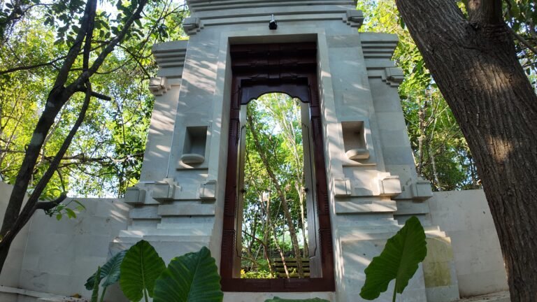 View through a traditional Balinese carved stone gate (angkul-angkul) at The Mahaloka entrance, surrounded by trees.