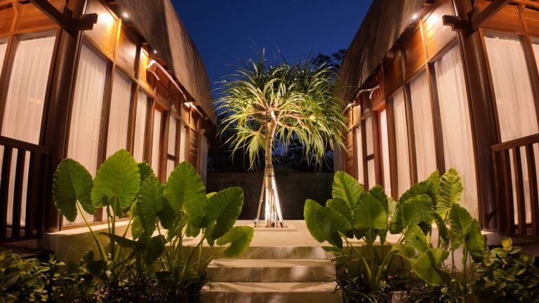 Symmetrical view down the central garden path between the two warmly lit lumbung villas at The Mahaloka at night.