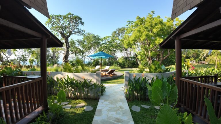 Symmetrical view down the stone garden path framed by the wooden decks of the two lumbung villas, leading towards the pool area.