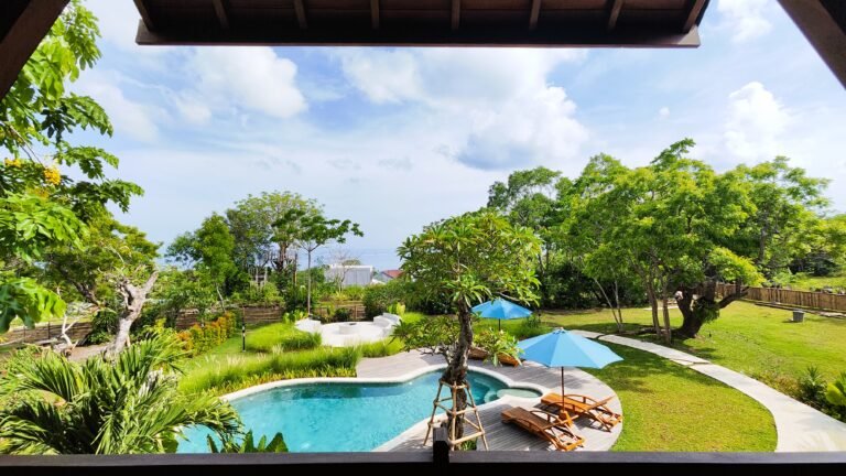 Panoramic view from The Mahaloka's king loft private balcony, overlooking the shared pool, lush gardens, and distant ocean horizon.