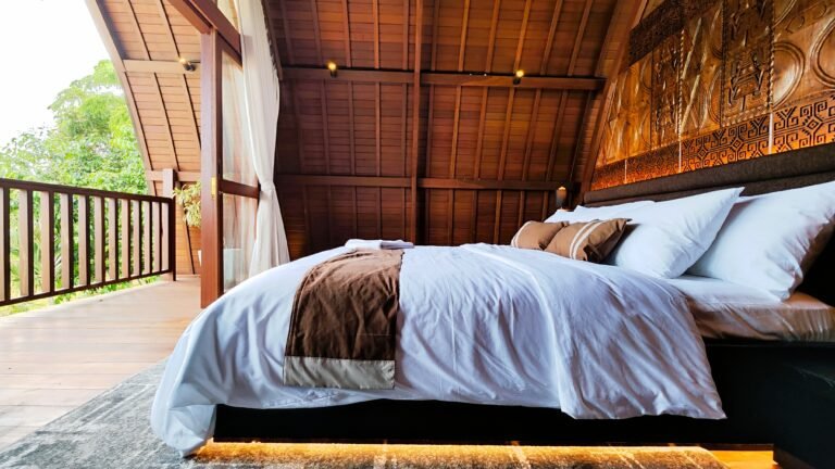 Low angle view of the plush king bed in The Mahaloka's lumbung loft, with carved headboard and view to the private balcony.