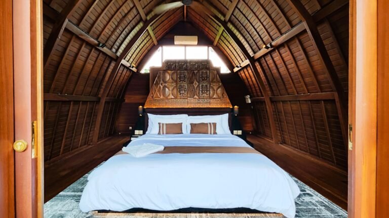 Symmetrical view of The Mahaloka king loft bedroom from the entrance, showing the bed, carved headboard, and high wooden ceiling.