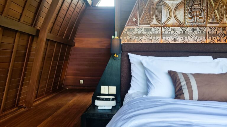 Close-up detail of the bedside table in The Mahaloka loft, showing lamp, power outlets, light switches, and headboard carving.