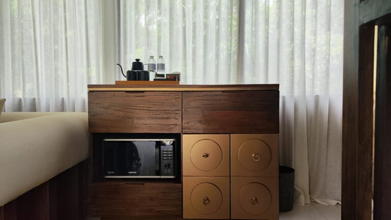 The wooden refreshment corner unit in The Mahaloka lumbung living area, showing microwave shelf and storage drawers.