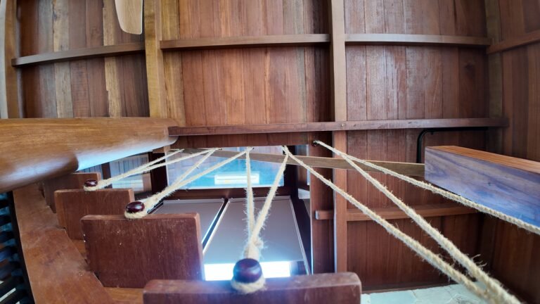 Close-up detail looking down the wooden stairs inside The Mahaloka lumbung, focusing on the unique rope railing design.