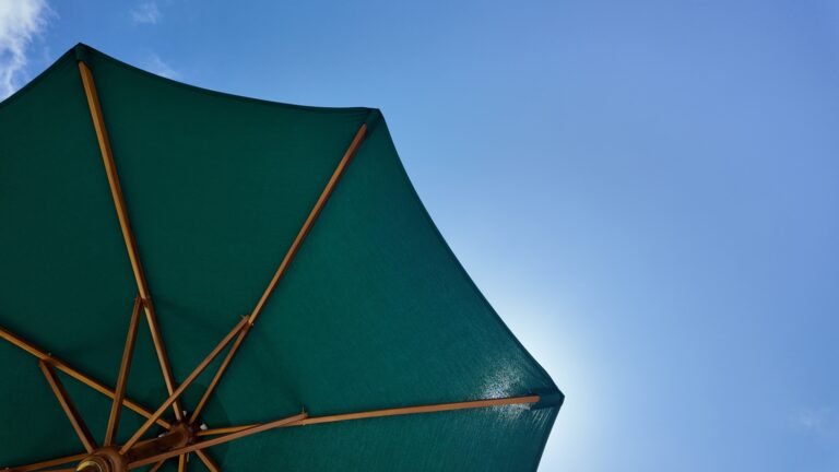 Low angle view across the turquoise shared pool at The Mahaloka, showing sun loungers, umbrellas, and mature trees.